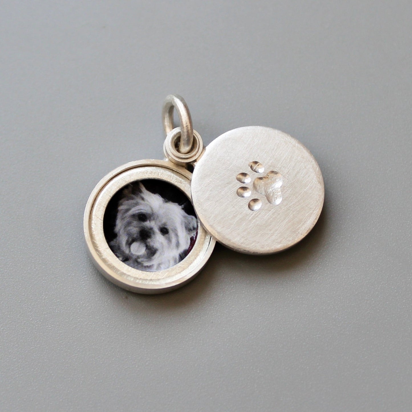 small silver locket decorated with a paw imprint showing a yorkshire terrier