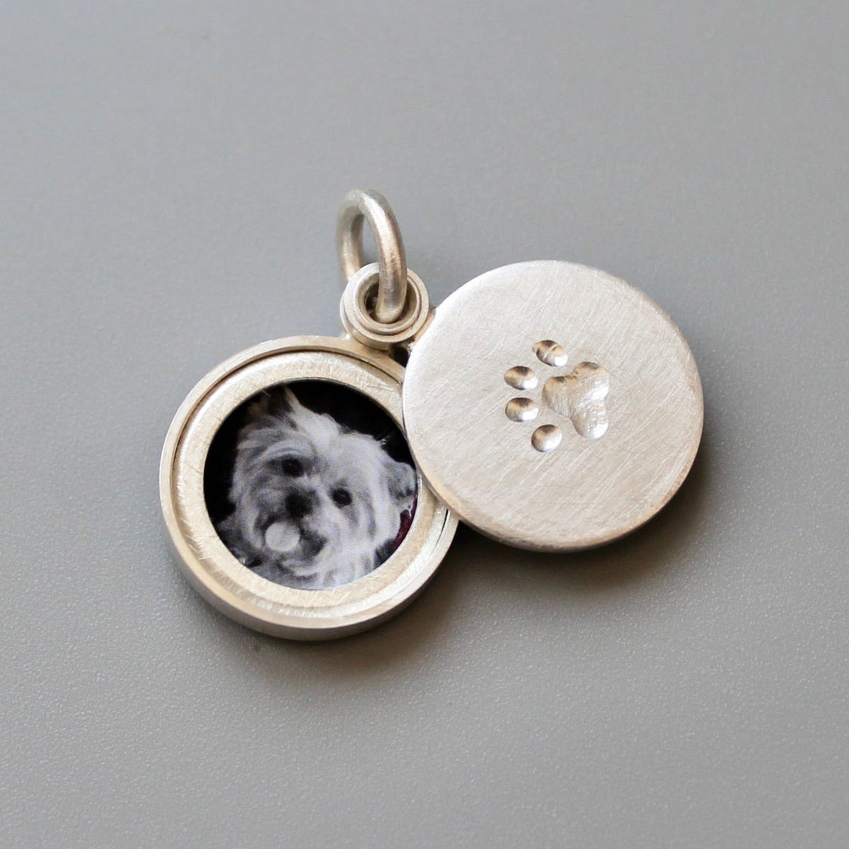 small silver locket decorated with a paw imprint showing a yorkshire terrier 