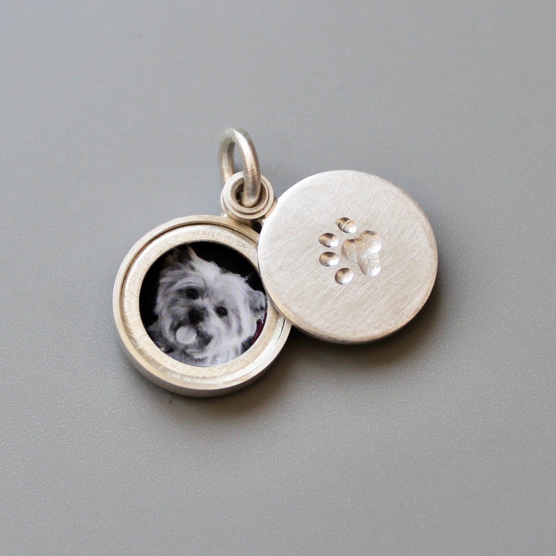 small silver locket decorated with a paw imprint showing a yorkshire terrier 