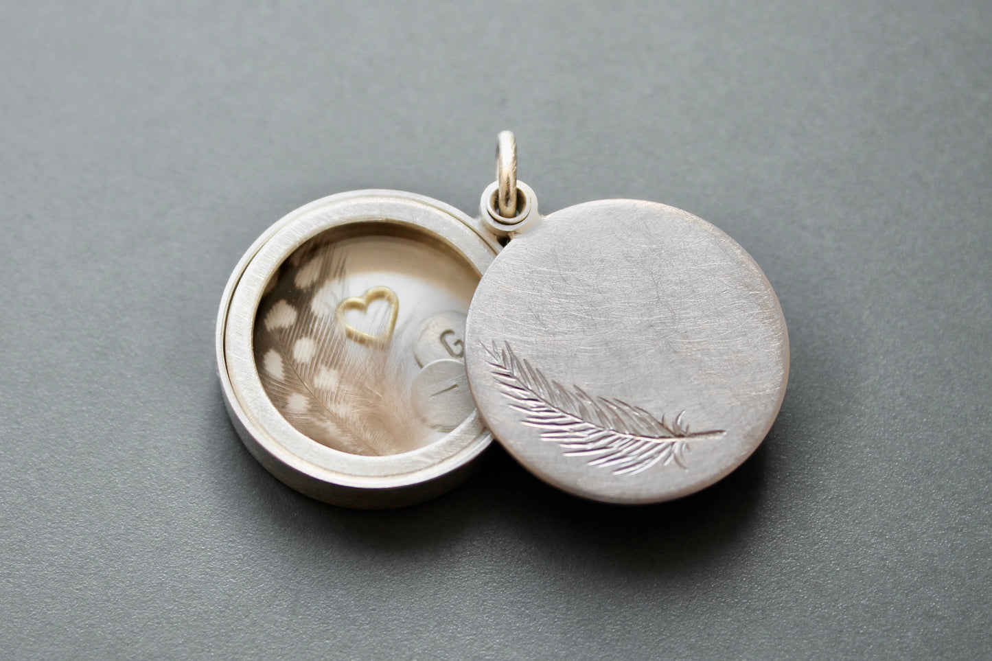 secret message locket filled with silver letter plates, a tiny feather and a golden heart